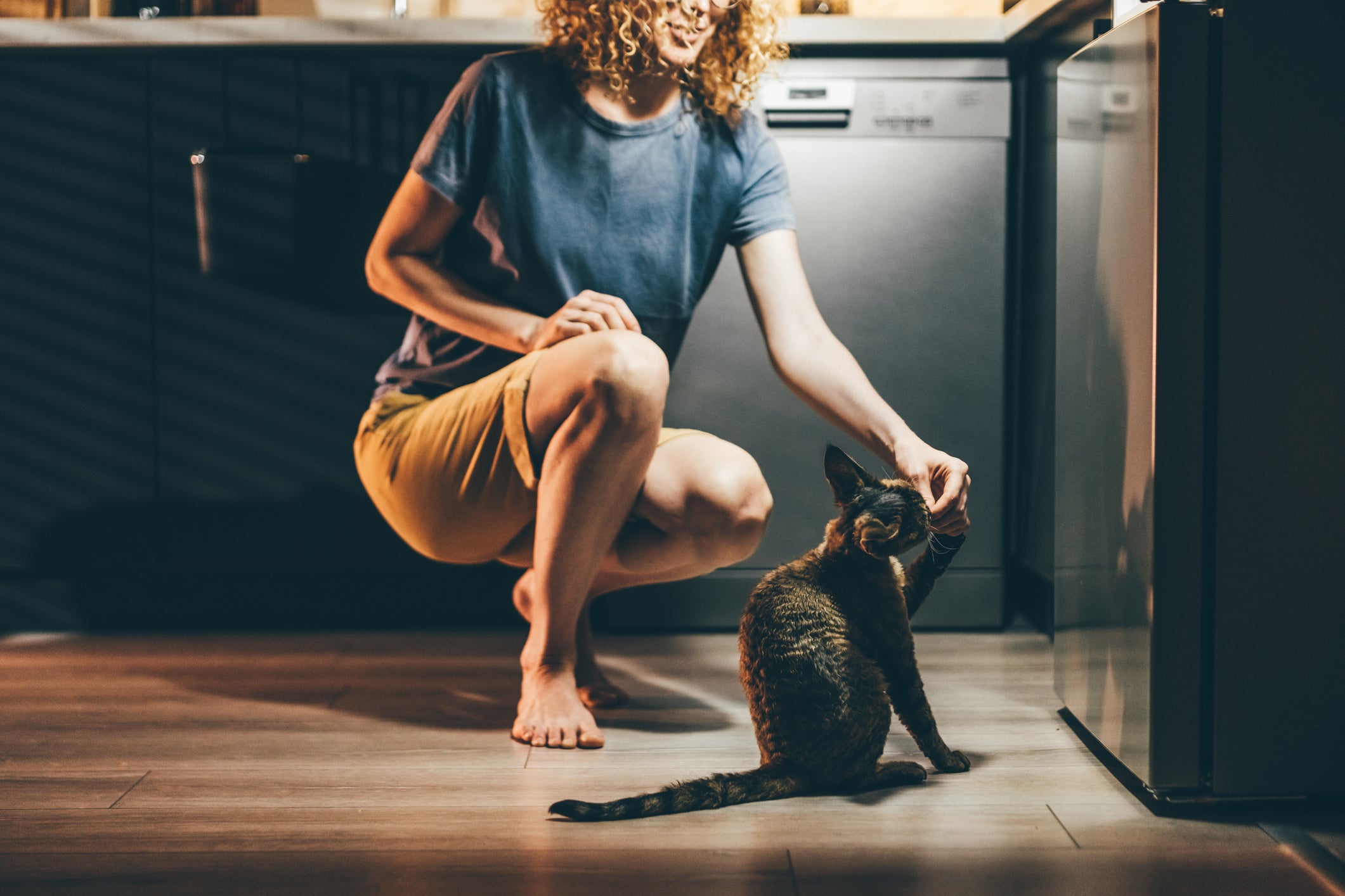 Tutora abaixada dando petisco para seu gato preto em cozinha