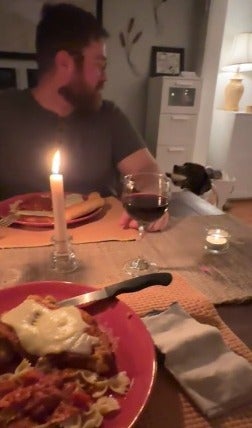 Homem sentado a mesa em jantar à luz de velas com um cachorro ao lado dele