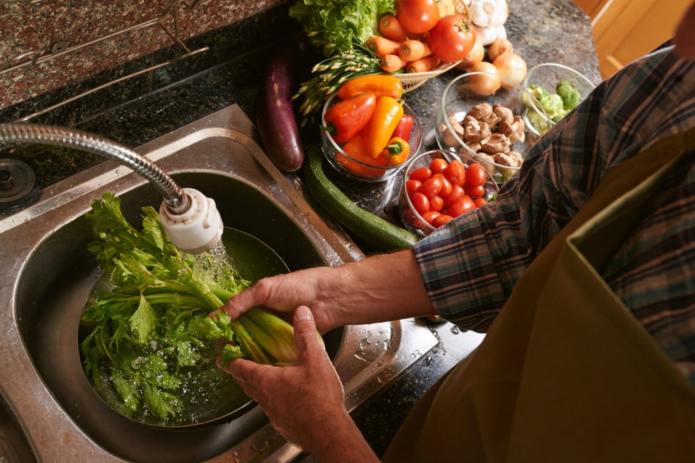 Mãos higienizando alface com vários legumes ao lado
