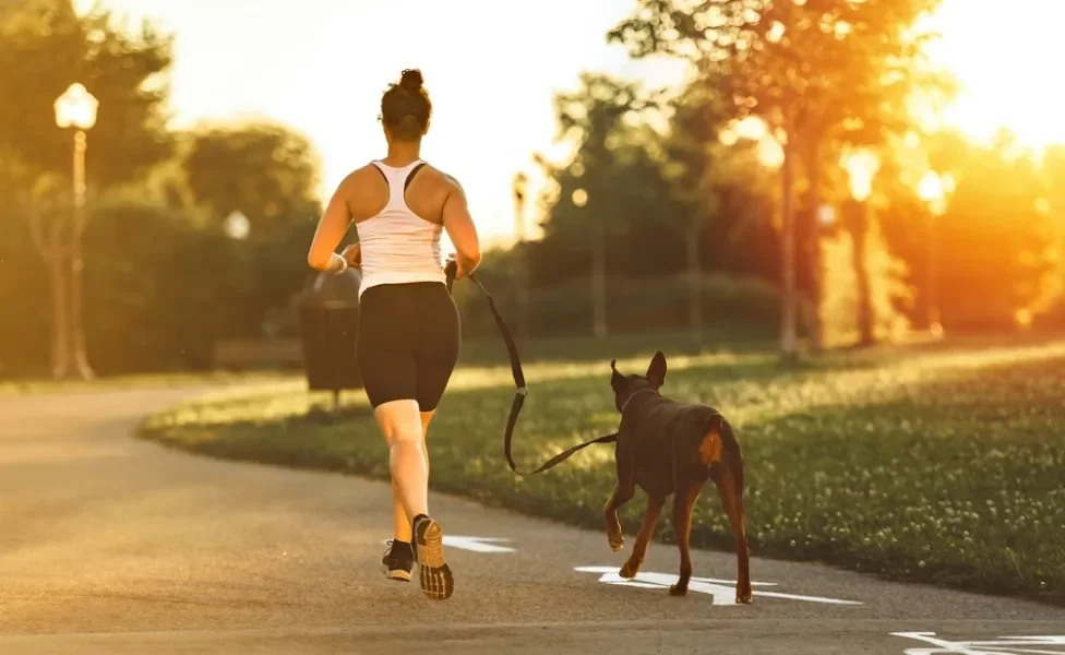 Mulher de costas correndo com cachorro na coleira